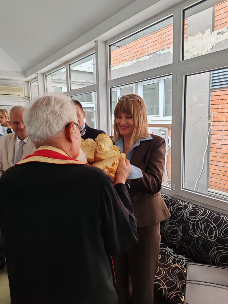 Pravoslavni sveštenik u crvenoj odeždi i direktorka Instituta za rehabilitaciju Snežana Kostić zajedno lome slavski kolač na slavi Sveti Vasilije Ostroški u Sokobanjskoj.